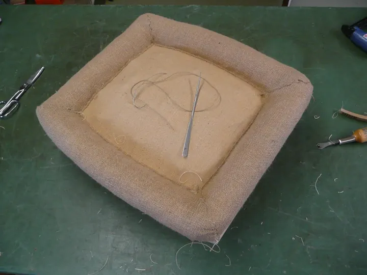 First step in the stuffing process is covering the springs with jute canvas. Wood wool is shaped into rolls around the frame.